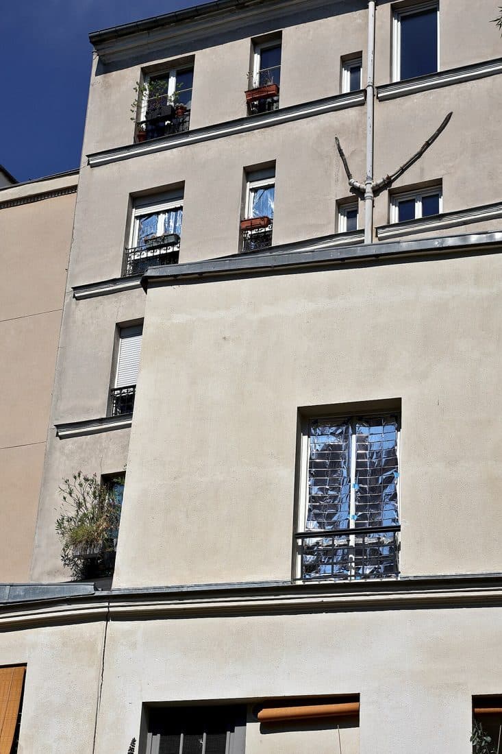Façade d’immeuble rue Henri-Chevreau à Paris, fenêtres couvertes contre le soleil